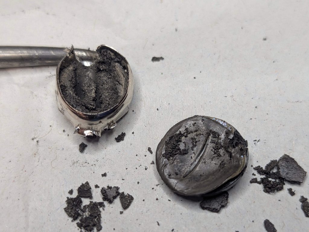 解体された使用済みボタン電池の缶と内部の黒い生成物
