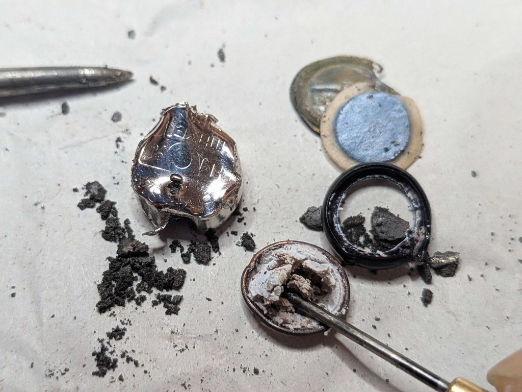 分解したボタン電池SR43SWの負極缶からピンセットで負極活物質をマイナスドライバーで剥がしている様子